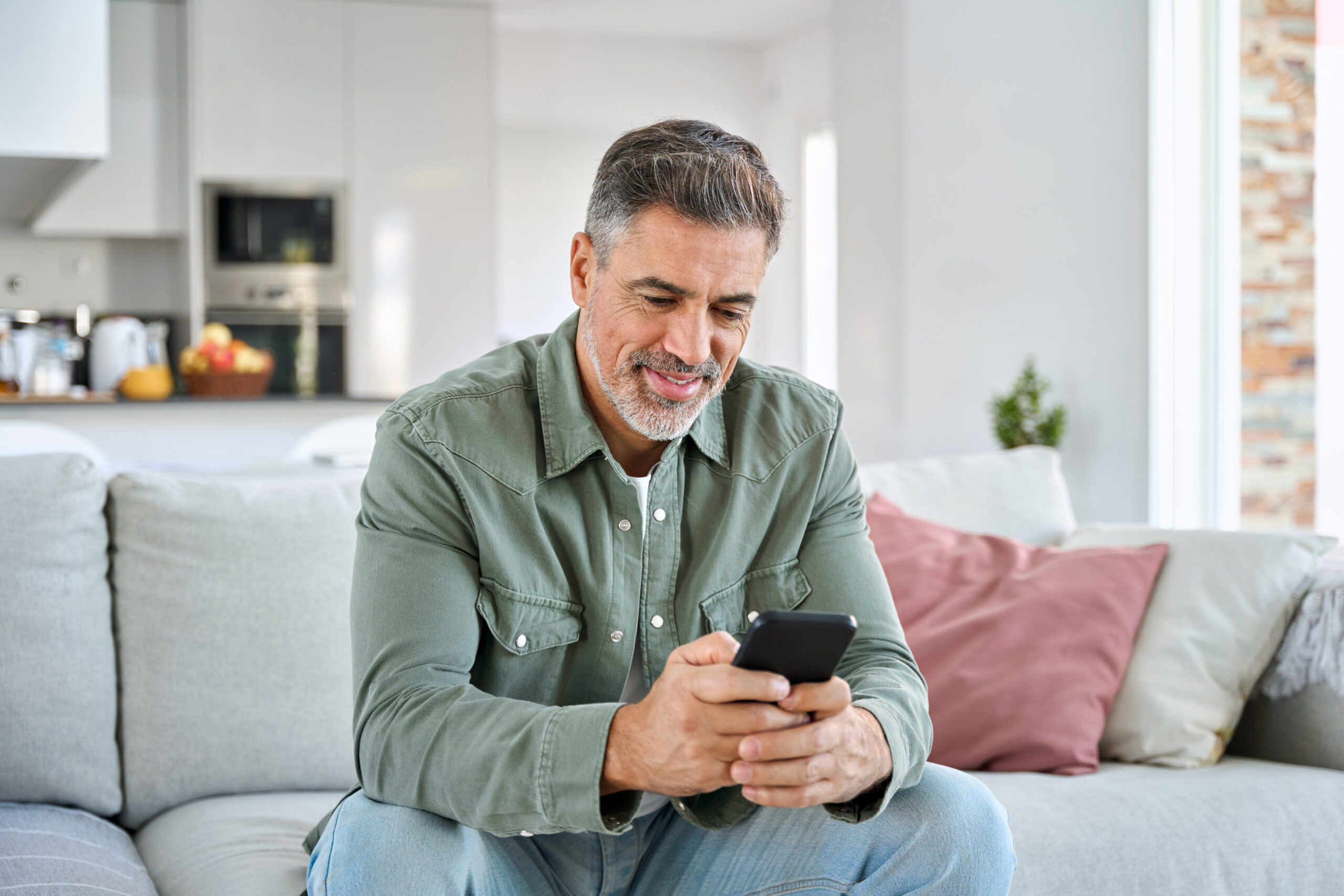 Middle aged old man using smartphone relaxing on couch at home.